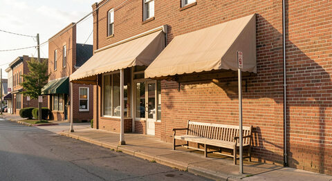 A plain brick storefront on a small-town Mississippi main street seen at an angle, a canvas awning and a wooden bench outside, bare wall with no sign, warm late afternoon light.