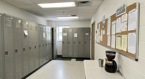 A break room in a Mississippi workplace with lockers, a notice board and a half-full coffee pot, no people, fluorescent light.