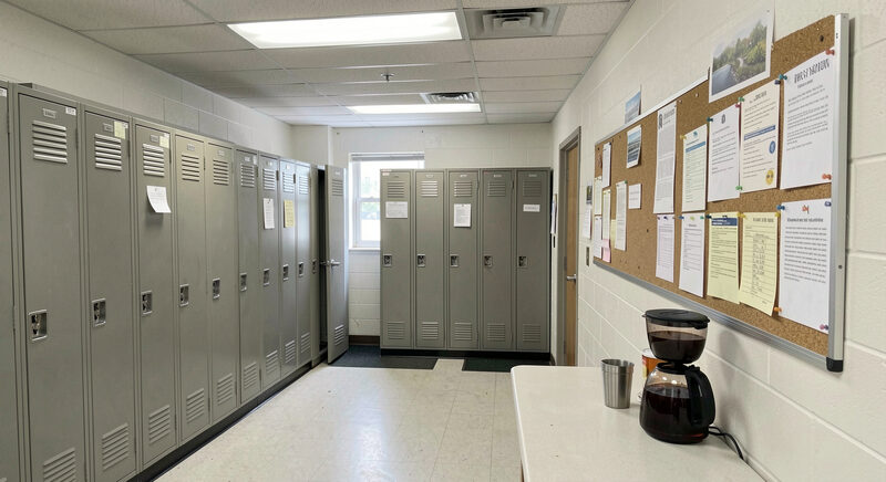 A break room in a Mississippi workplace with lockers, a notice board and a half-full coffee pot, no people, fluorescent light.